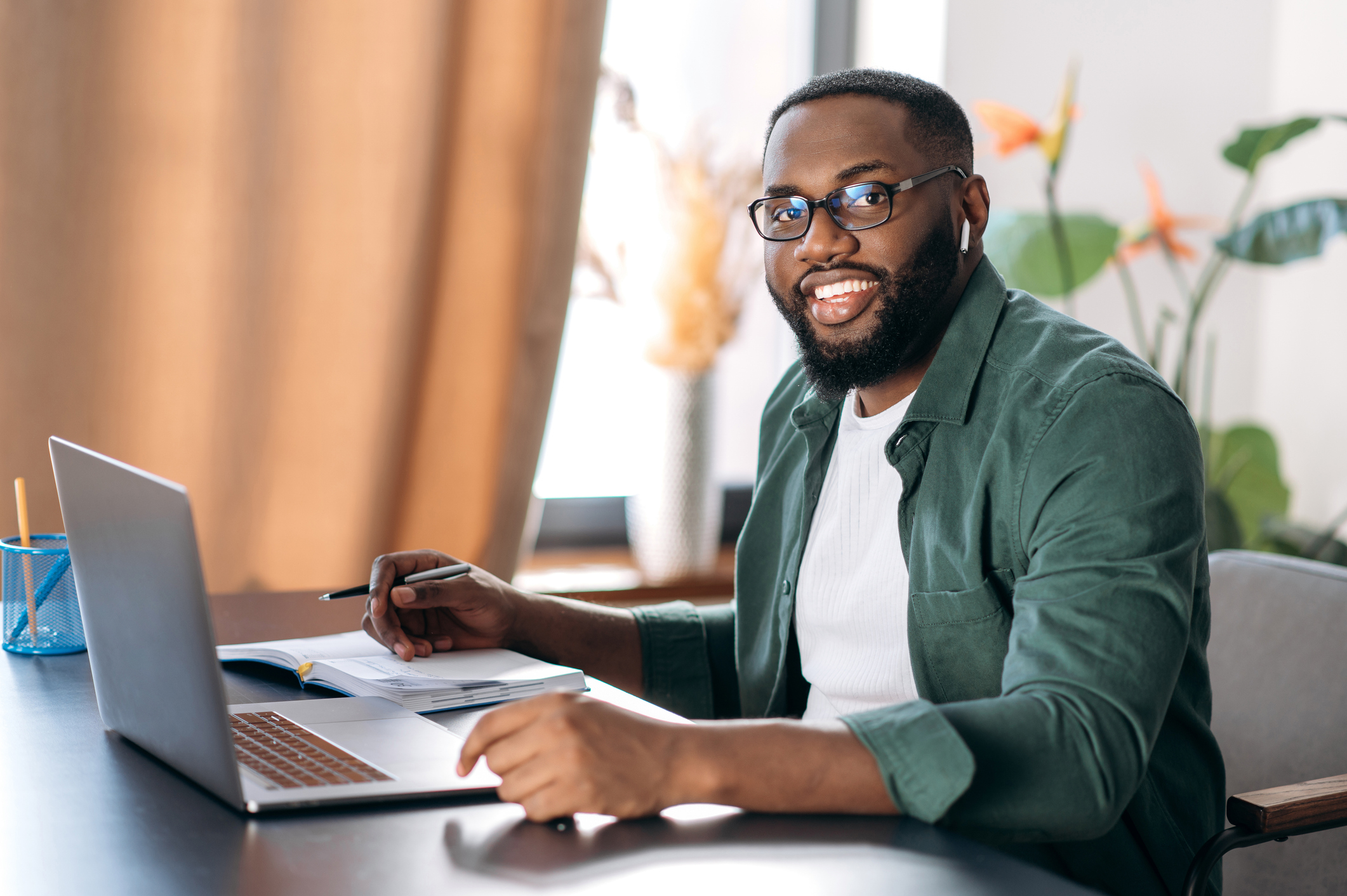 Homem negro usando óculos sorri em frente a um computador